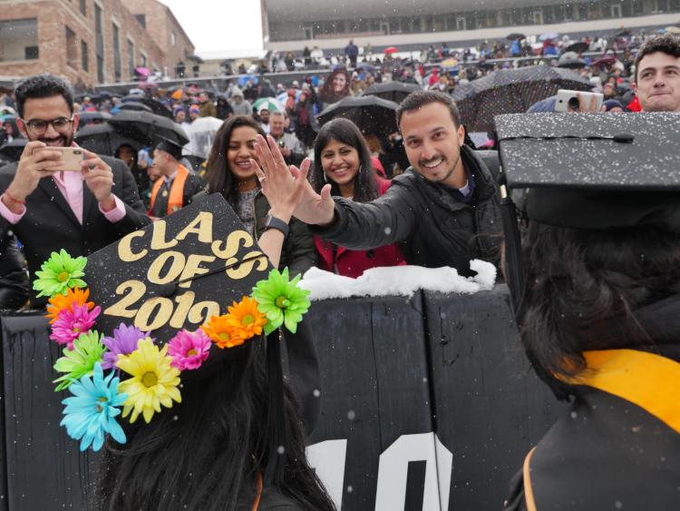 Graduates say hi to family members in the stands of Folsom Field
