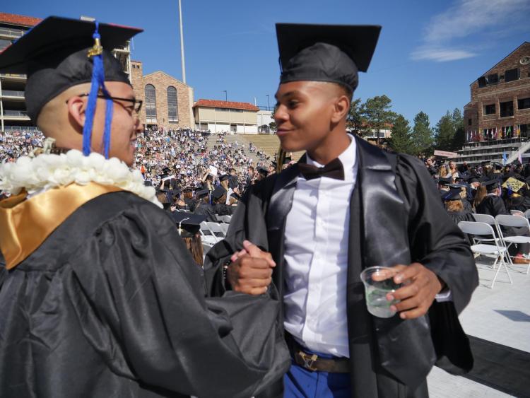 Two graduates shake hands on Folsom Field before the commencement ceremony. Photo by Glenn Asakawa.