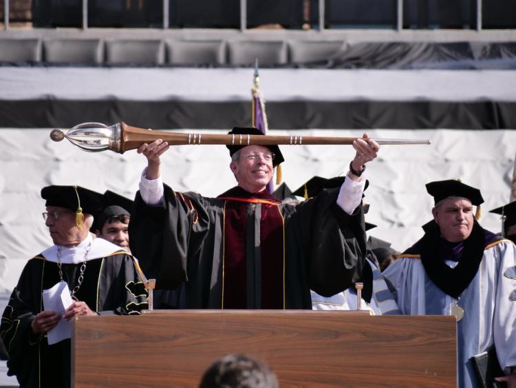 Bud Coleman, chair of Theatre & Dance and commencement marshal, lowers the staff signaling the start of the ceremony. Photo by Glenn Asakawa.