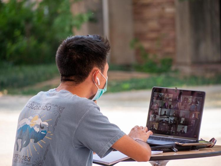 student joins virtual event on laptop outside