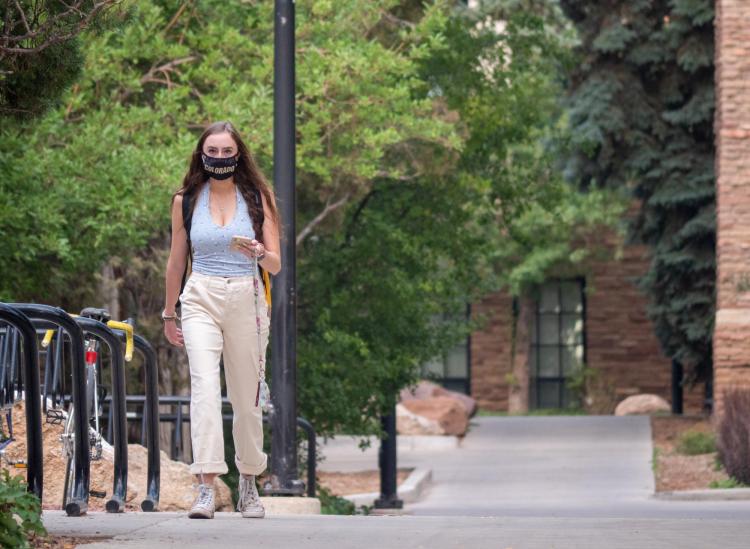 Student walking on campus while wearing a mask