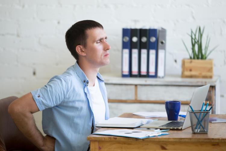 Man rubs back while sitting at desk