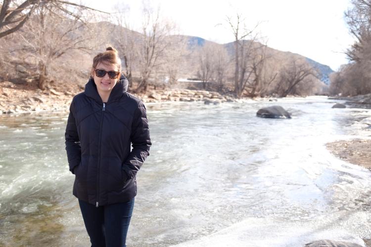 Elizabeth Koebele stands in her winter coat with the Arkansas River in the background.