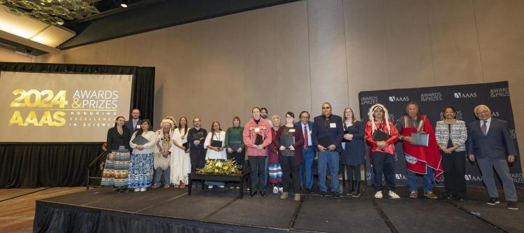 People line up on a stage with a screen displaying the words "2024 AAAS"