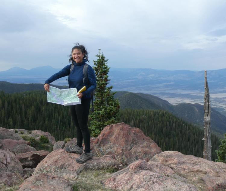 Sabrina Kainz holds up a map while standing on a rocky overlook