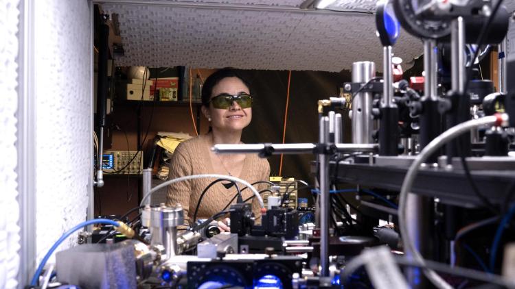 Ana Maria Rey wearing safety glasses sits amid scientific equipment