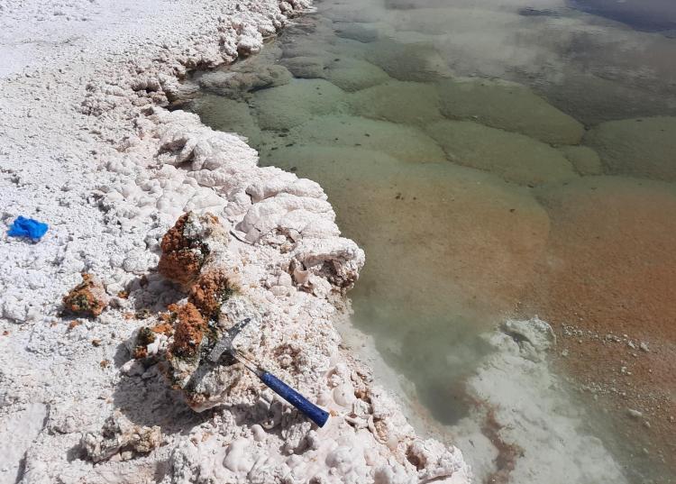 A rock hammer sits on top of a cracked open chunk of minerals next to a lagoon