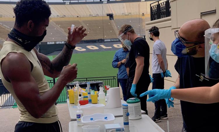 CU Boulder athlete holds up a vial for testing his saliva for the coronavirus.