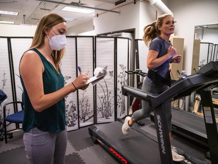 A runner runs on a treadmill while a researcher looks on