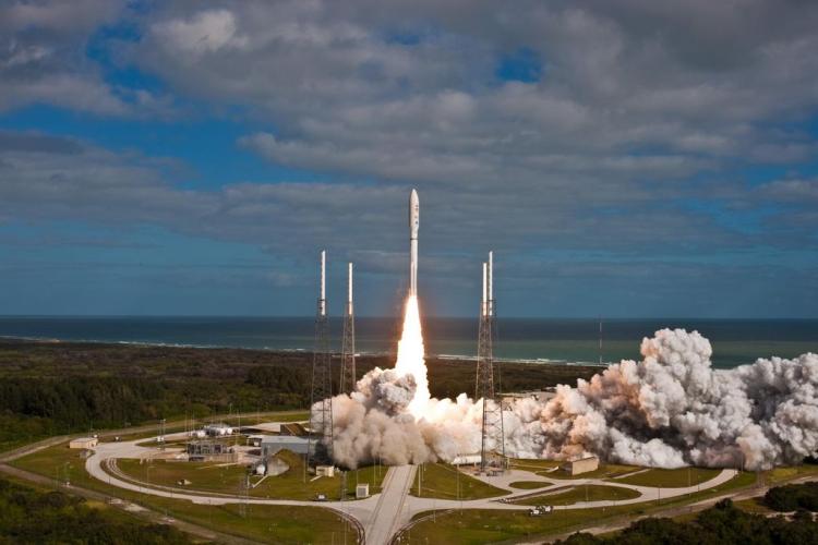 The Atlas V rocket takes off from a launch pad.