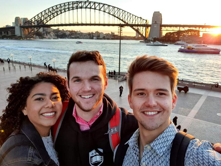 Three students take a photo by the Harbour Bridge in Sydney, Australia