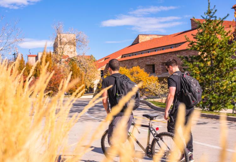 Two students walk their bikes to class during a beautiful autumn day on campus. Photo by Patrick Wine.