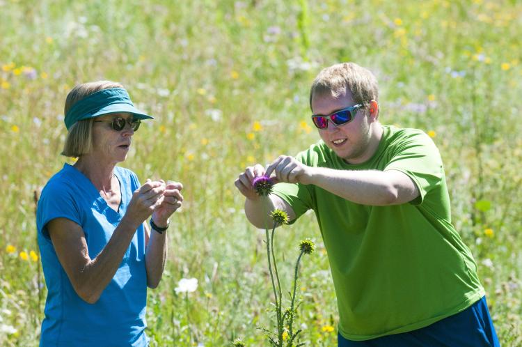A student and a teacher lift a bee off of a flower