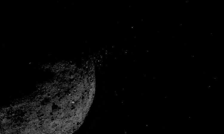 Image of the asteroid Bennu with small bits of material jumping off into space.