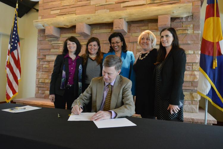Gov. John Hickenlooper signs bill with people looking on.