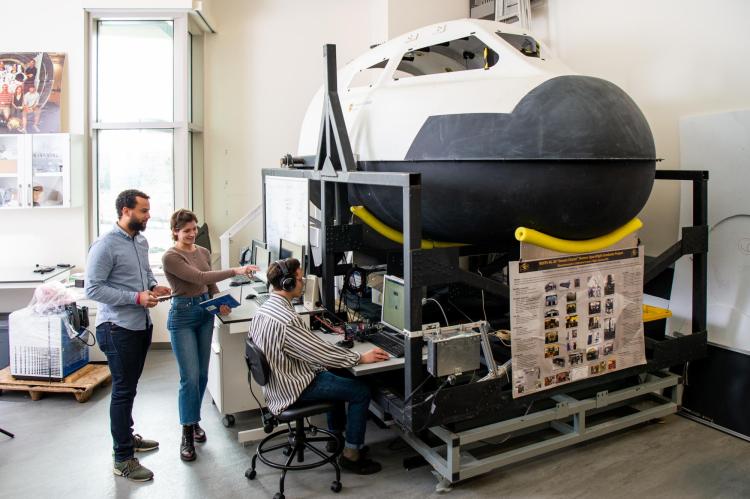 Graduate students stand in front of a full-sized model of the nose of a space shuttle.