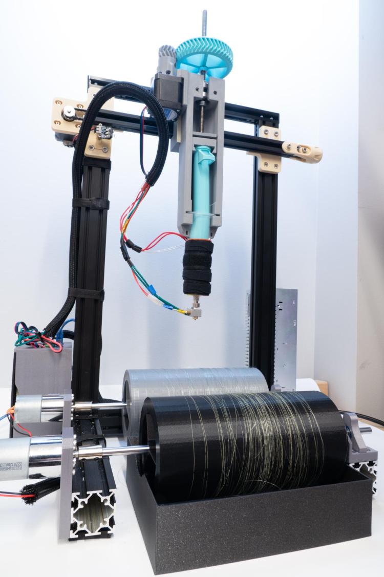 Machine sits on a tabletop with a long, plastic syringe mounted above two spinning wheels