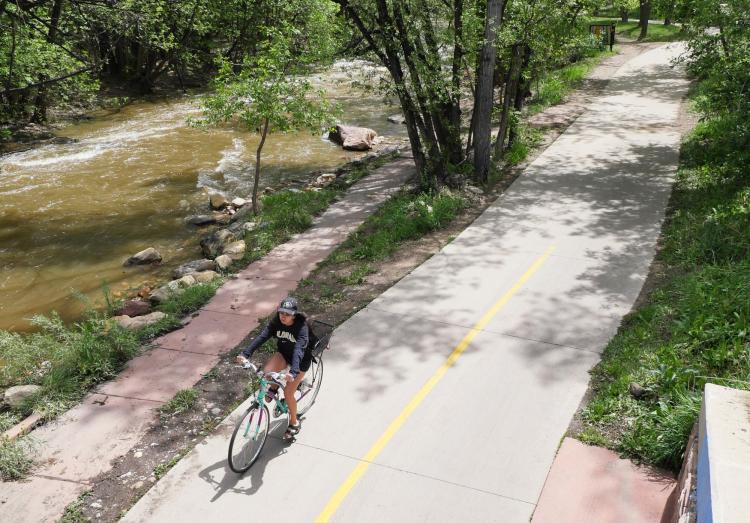 A student rides their bike along Boulder Creek
