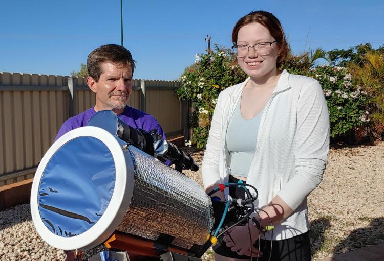 Man and woman stand behind a telescope on a sunny day