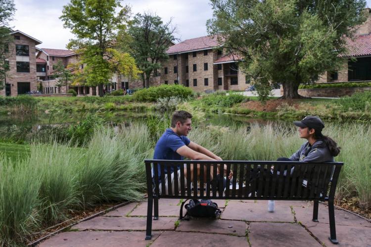two students sit on a bench on campus, talking