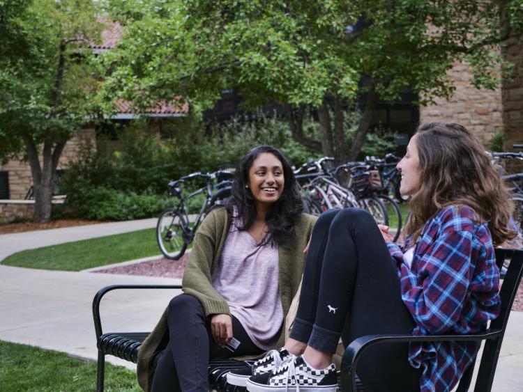 Two students sit on a bench talking