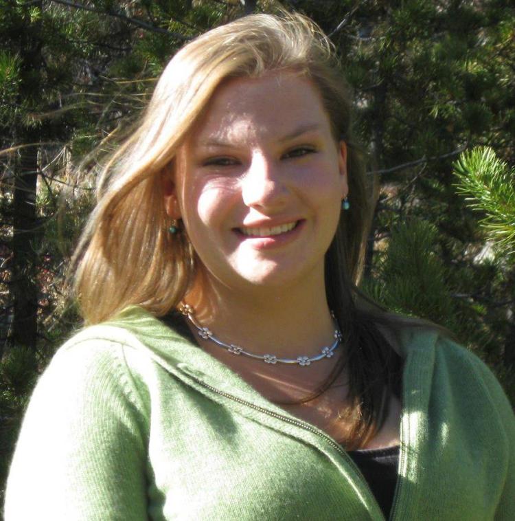 Portrait of Charlotte Truesdell wearing a green sweater with green trees in the closebackground.