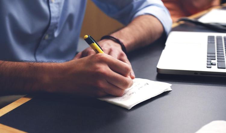 Person writes in notebook with laptop nearby