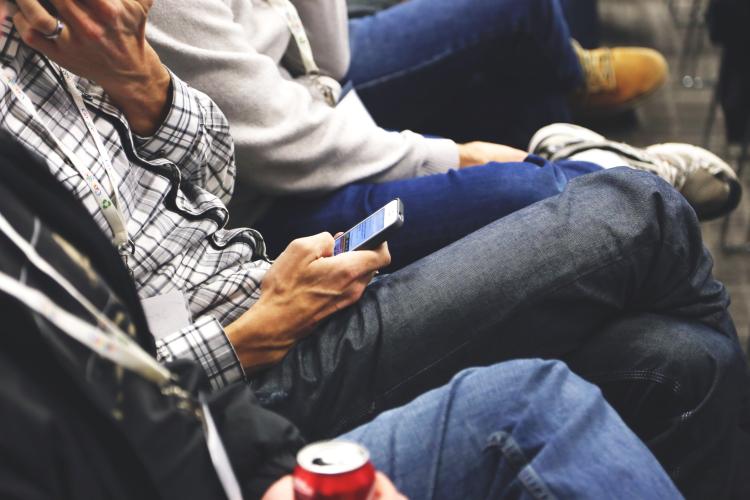 A person sits in a row of event attendees, checking their mobile phone