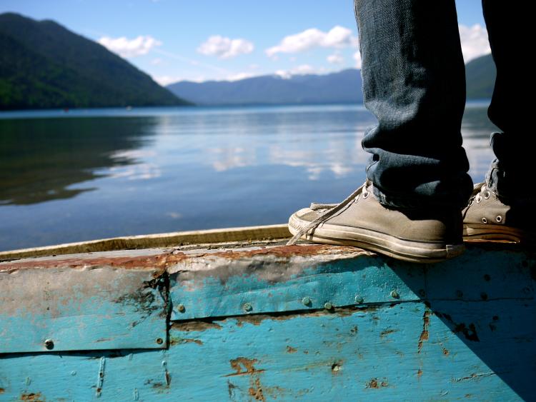A close-up of someone's feet in Converse tennis shoes are seen on the edge of a dock looking out over a body of still water surrounded by mountains in Chile. Photo by Keenan Fitzpatrick.