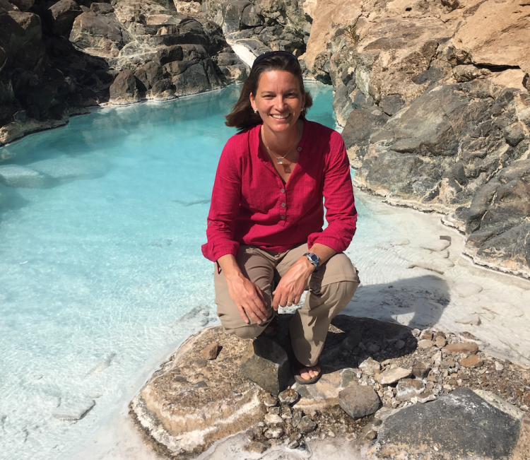 Woman kneels on a rock amid a vibrant blue pool of water
