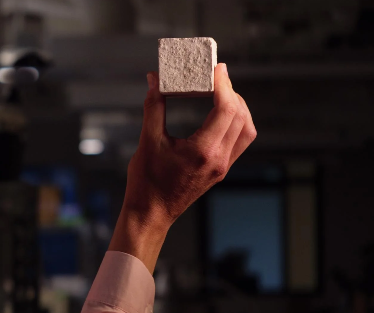 Hand holds up a cube made from what looks like sand