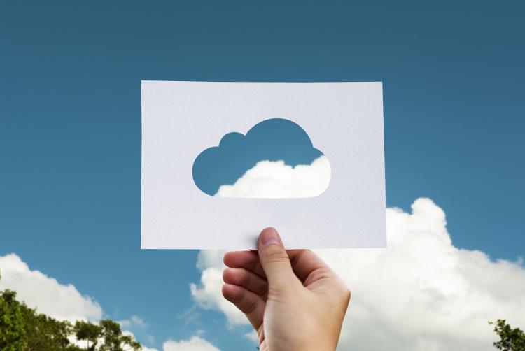 Person holds up paper cutout of cloud with sky, clouds in background