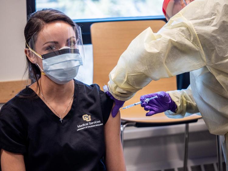 A nurse gives a woman a vaccine shot in the shoulder.
