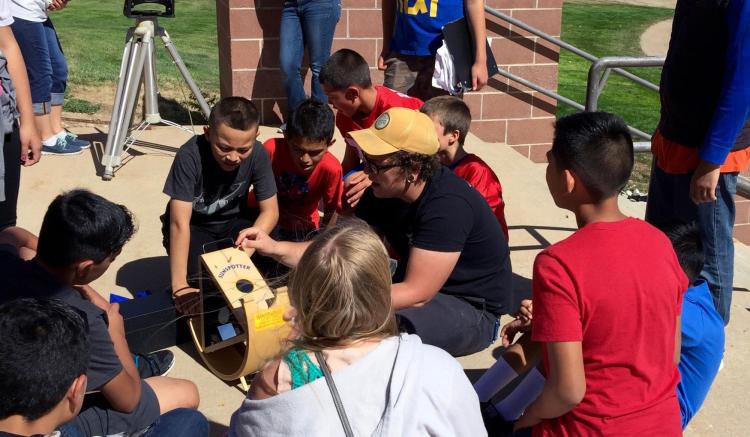 Young students gather around a CU-STARS volunteer with sun spotter device