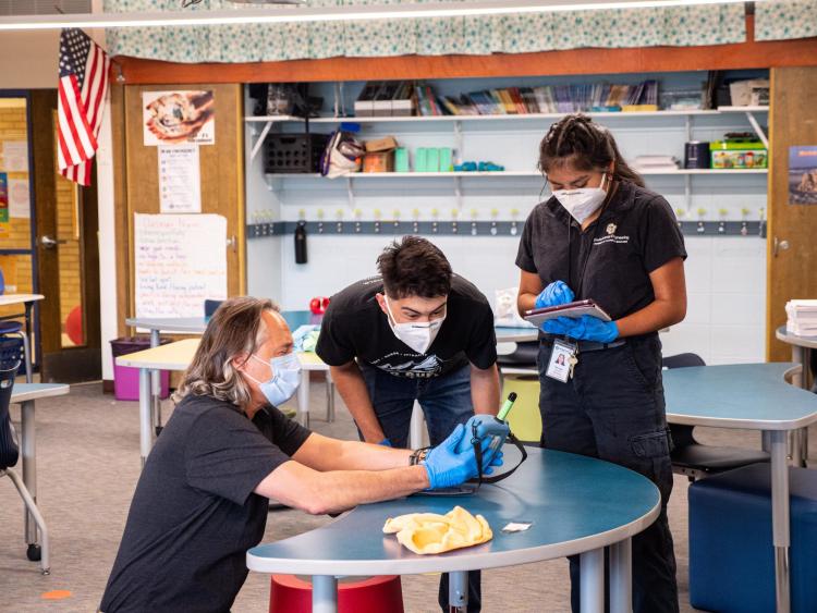 Mark Hernandez, Ricardo Reyes and Halle Sago monitor the microbe levels on a classroom desk