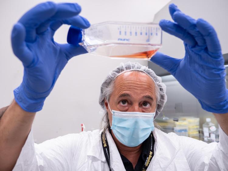 Mark Hernandez, wearing protective gear, inspects a flask filled with liquid