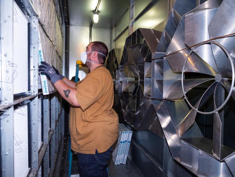 Maintenance worker switches out filters next to a giant fan