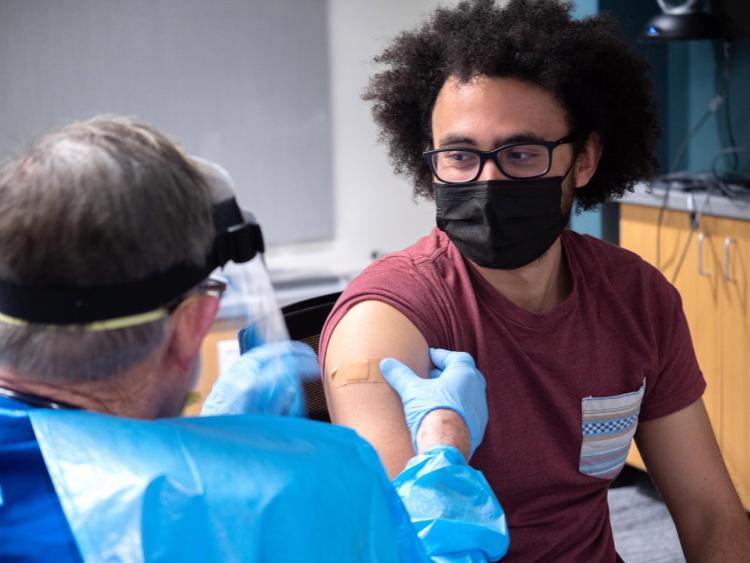 Student gets a vaccine from a doctor wearing a gown and face protection