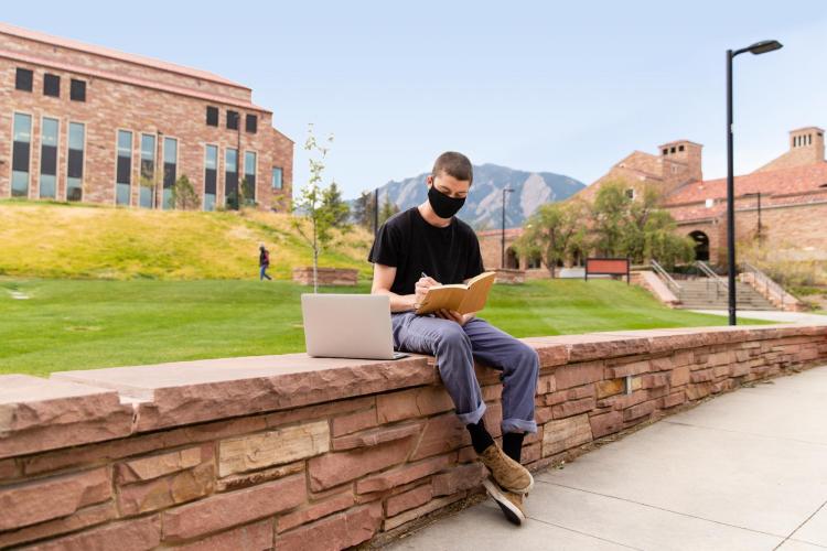 Student wearing mask working on laptop outside