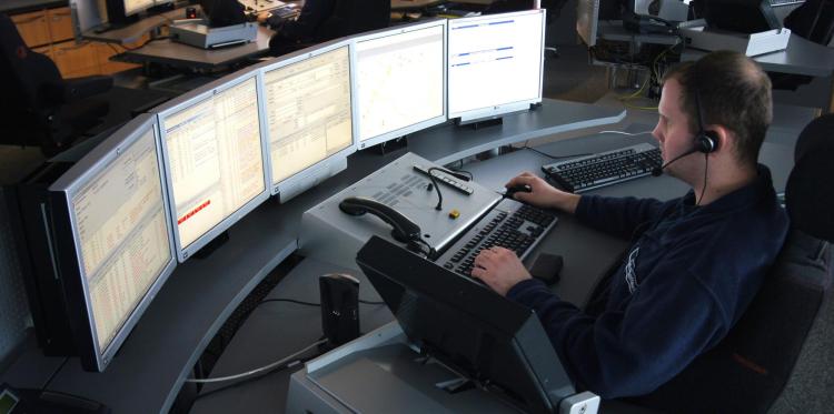 Dispatcher sits at desk with five computer monitors