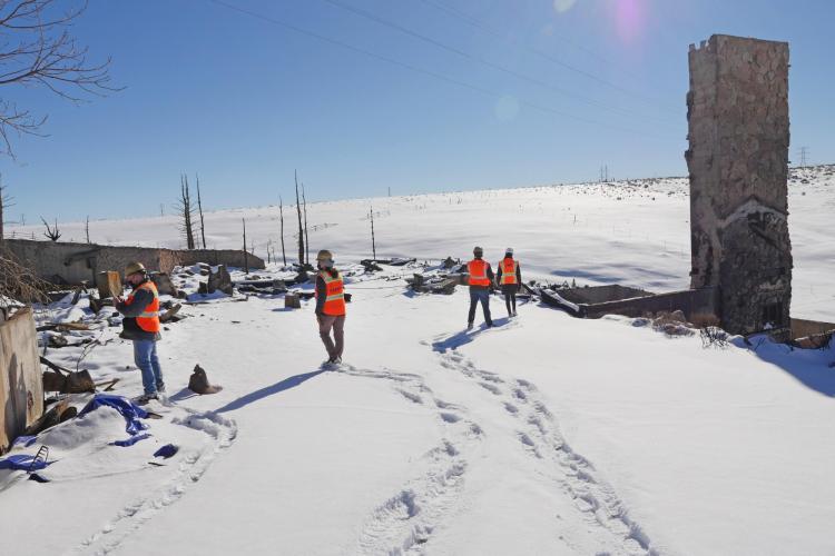 Researchers in safety vests walk through a snowy lot next to a stone chimney