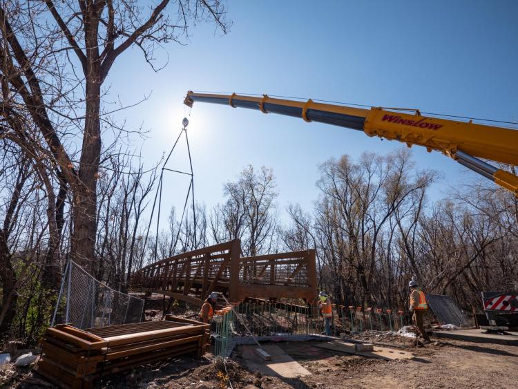 Workers use a mobile crane to place a 33-ton bridge over Boulder Creek on East Campus. Photo by Glenn Asakawa.