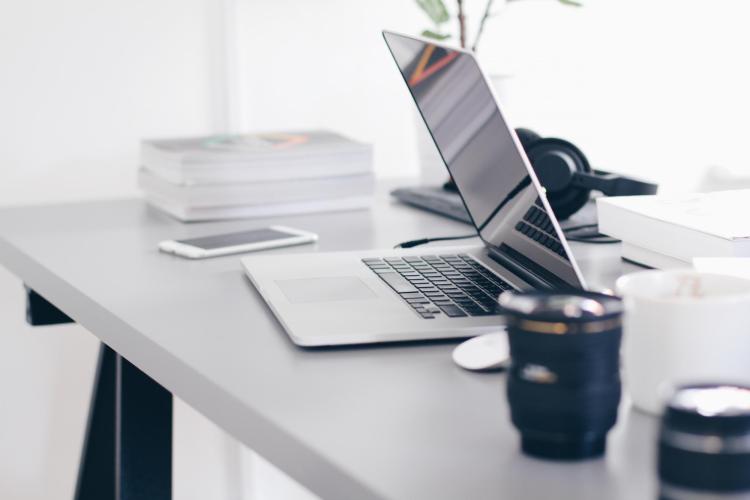 Unattended desk with laptop, camera lenses, mobile phone, headphones