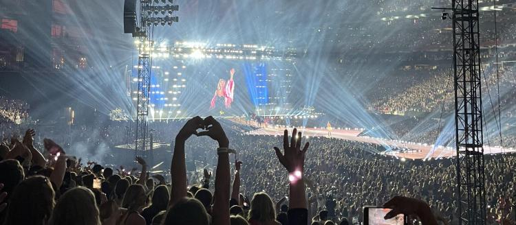 crowd shot during a concert with someone making a heart shape with their hands