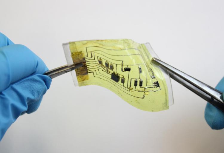 An "electronic skin" device is held from either side by forceps.