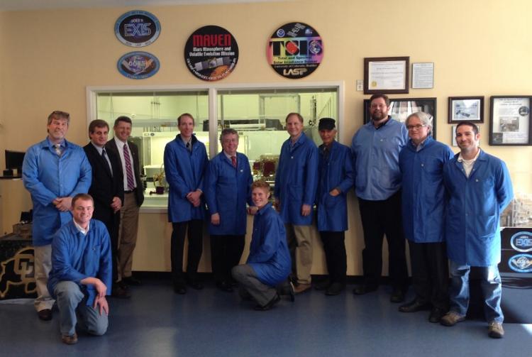 Row of people in blue coats pose for a photo in front of a window