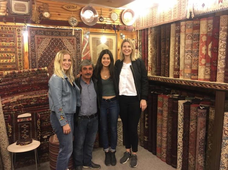 Three female college students pose with owner of carpet shop in Istanbul, Turkey