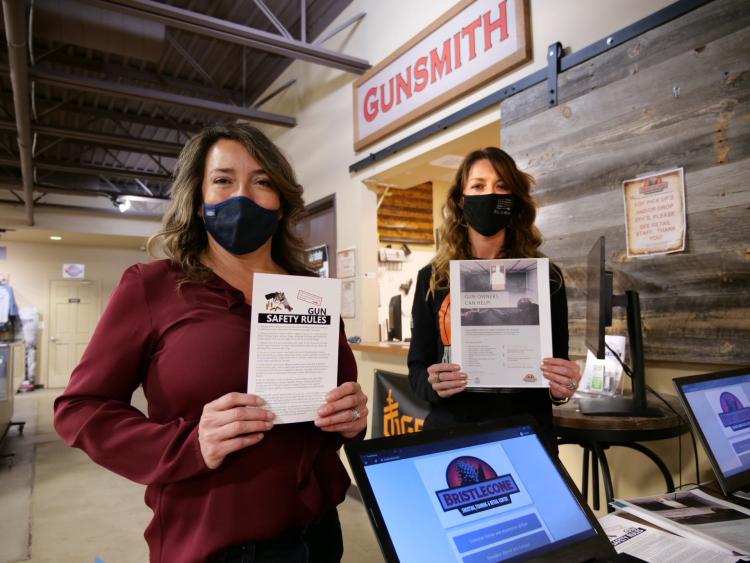 Two women hold up educational materials near a set of cash registers