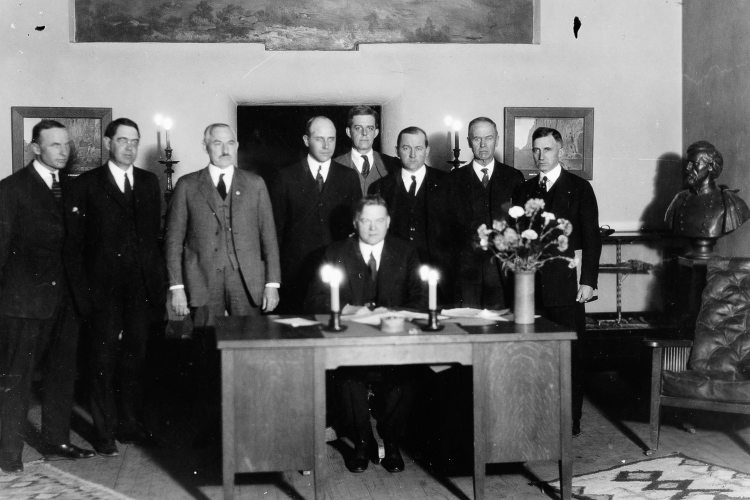 Eight men pose for a photo around a desk