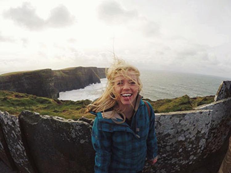 A person poses for a photo near cliffs and water.